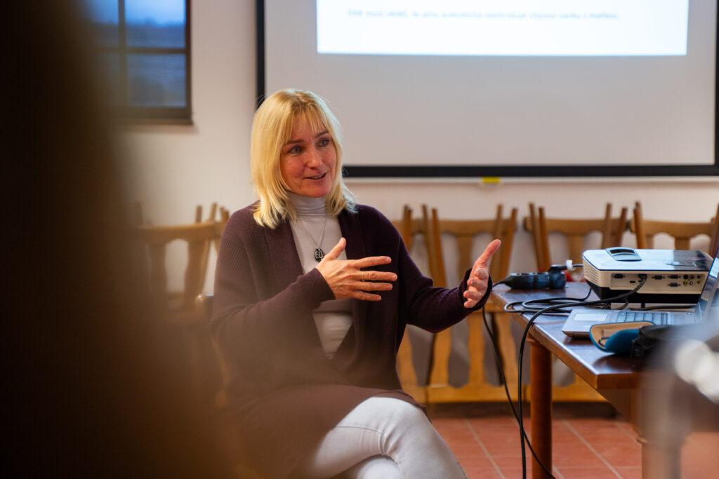 Skupina interních a externích spolupracovníků Kliniky NAU během setkání v Mendelově domě ve Vražném v roce 2025, poslouchající přednášku Pavly Sabolové